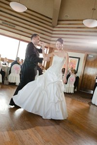 Wedding couple mid-dance, with the groom lifting the bride's hand high, preparing for an elegant underarm turn in their dance routine.